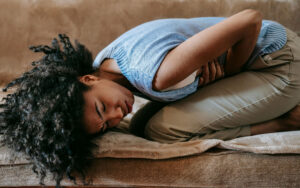 An African woman doubled over in pain on the couch affecting her mental health