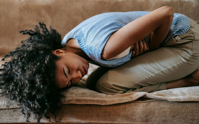 An African woman doubled over in pain on the couch affecting her mental health